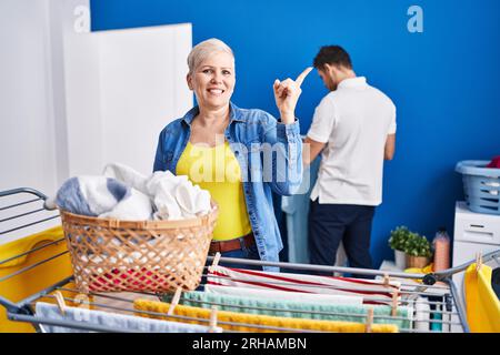 Hispanische Mutter und Sohn hängen Kleider an der Wäscheleine auf und lächeln fröhlich mit Hand und Finger zur Seite Stockfoto