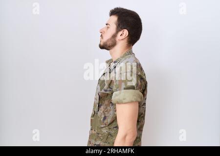 Junger lateinamerikanischer Mann in Tarnuniform, die zur Seite schaut, entspannt mit natürlichem Gesicht und selbstbewusstem Lächeln posiert. Stockfoto