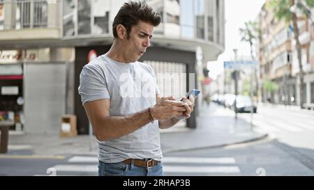 Junger hispanischer Mann, der ein Smartphone benutzt, überrascht von der Straße Stockfoto