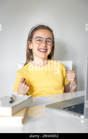 Süßes Schulmädchen mit einem Laptop, das zu Hause lernt, online lernt. Stockfoto