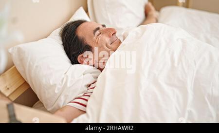 Ein Mann mittleren Alters, der im Schlafzimmer Arme streckt Stockfoto