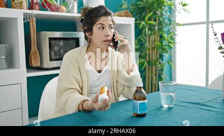 Junge schwangere Frau, die eine medizinische Beratung durch Smartphone mit Pillen im Speisesaal Stockfoto