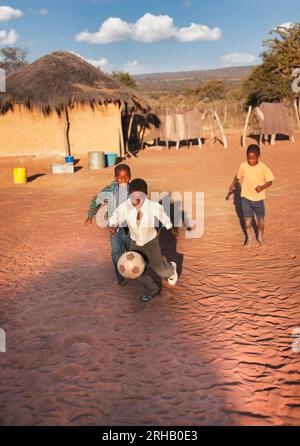 Afrikanische Dorfkinder, die auf dem Dreck im Hof Fußball spielen Stockfoto
