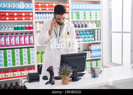Junger arabischer Apotheker, der in der Apotheke am Computer auf dem Smartphone spricht Stockfoto