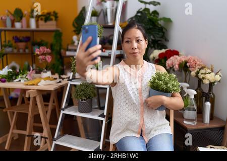 Eine junge asiatische Floristin macht Selfie mit einer Smartphone-Holding-Pflanze im Blumenladen Stockfoto