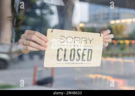 Weibliche Ladenbesitzerin, die das Schild des Start-up-Cafés und Restaurants durch die Tür dreht und den täglichen Service schließt Stockfoto