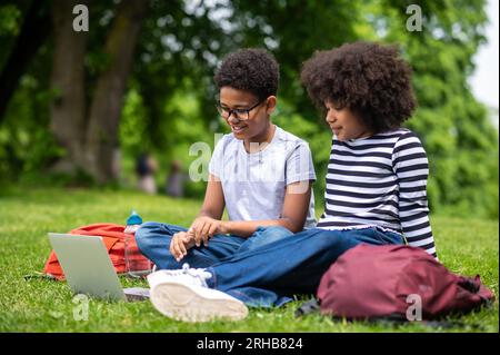 Zwei afroamerikanische Kinder sitzen auf dem Gras im Park Stockfoto