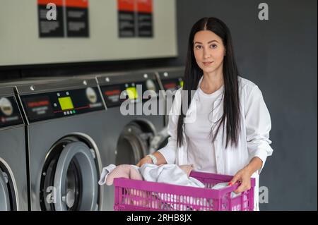 Eine junge Frau wäscht wöchentlich in einem Waschsalon. Stockfoto