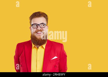 Rotbärtiger, molliger Mann in Brille und funky Outfit, der auf den Kopierraum auf gelbem Hintergrund schaut. Stockfoto