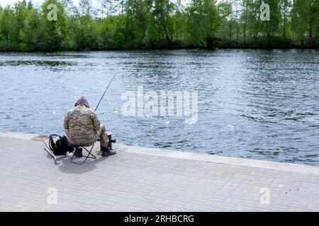 Ein Fischer mit einer Angelrute sitzt auf einem Stuhl auf dem Pier Stockfoto