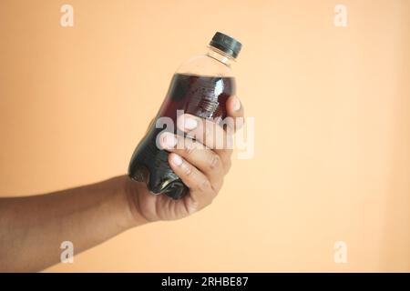 Männer, die eine Plastikflasche mit Erfrischungsgetränk vor orangefarbenem Hintergrund halten Stockfoto