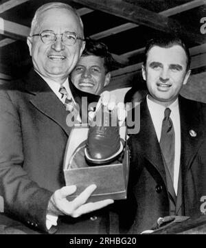 Brockton, Massachusetts: 18. Oktober 1952 Präsident Truman zeigt ihm ein Paar Schuhe, die ihm Bürgermeister Lucey (r) in diesem Schuhzentrum überreicht hat, während der Präsident seine Whistle-Stop-Tour durch Neuengland in seiner Kampagne für den demokratischen Kandidaten Adlai Stevenson fortsetzte. John F. Kennedy, der in der Pressemitteilung nicht erwähnt wurde, steht im Hintergrund. Stockfoto