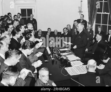 Washington, D.C.: 8. Mai 1945 Präsident Truman, als er die Siegesproklamation vor dem Pressekorps liest, die offiziell das Ende des Krieges in Europa verkündet. Im Hintergrund versammelt sich L-R: Elmer Davis (von Hand an Kopf); Handelsminister Henry A. Wallace; Generalmajor Philip Fleming; Rep. Joseph Martin; General der Armee George C. Marshall; J. Leonard Reinsch; Oberst Harry Vaughan; John W. Snyder; Mrs. Truman; Margaret Truman und Kriegsminister Henry L Stimson. In der Mitte des Vordergrunds, der in die Kamera schaut, ist Fred M. Vinson. Stockfoto