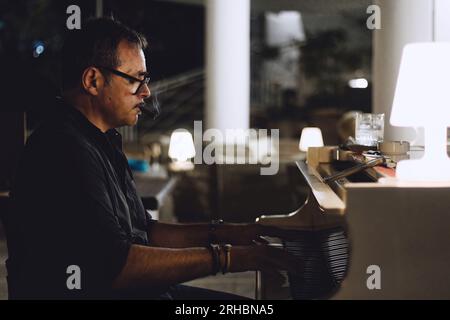 Ein männlicher weißer Kaukasier mittleren Alters spielt leichten Jazz in einer Piano-Lounge für eine Party und raucht eine Zigarre Stockfoto