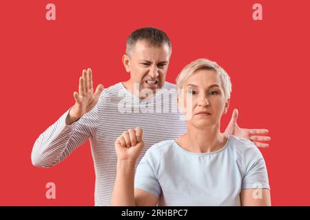 Reife Frau mit geballter Faust und ihrem streitenden Ehemann auf rotem Hintergrund Stockfoto