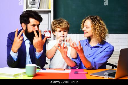 Niedliche Schülerin, die Mathematik lernt und mit den Eltern auf die Finger zählt. Kleines Kind, das mit Lehrern Mathe-Hausaufgaben macht. Junge aus der Grundschule mit Eltern Stockfoto