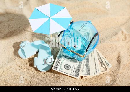 Sparschwein mit Strandzubehör und Geld auf Sand. Konzept der Ersparnisse bei Reisen Stockfoto