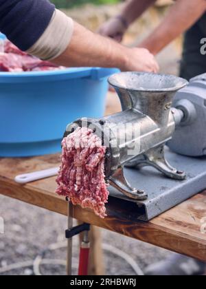 Selektiver Fokus des Metallfleisches mit Forcemeat auf dem Holztisch auf männliche Feldfrüchte mit Schüssel aus gehacktem Fleisch in der Natur Stockfoto