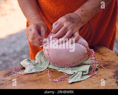 Unbekanntes reifes Weibchen in einer Schürze, die frische traditionelle Sobrassada-Wurst mit Faden verbindet, während sie an einem sonnigen Tag auf Mallorca in der Metzgerei arbeitet Stockfoto