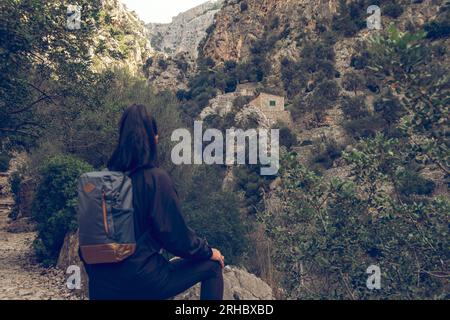 Rückblick auf eine nicht wiedererkennbare Touristin mit Rucksack, der am Rande des weißen Hügelkliffs ruht und zum Biniaraix-Dorf Soller in Mallorc reist Stockfoto