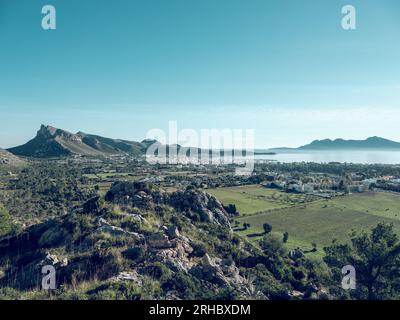 Malerischer Blick auf die Stadt Pollensa inmitten grüner landwirtschaftlicher Felder und Berge am blauen Himmel an der Meeresküste von Mallorca, Spanien Stockfoto