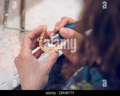 Von oben nach oben bei der pflanzanonymen Kieferorthopädin-Kieferorthopädin mit Drehmaschine beim Polieren von nicht abnehmbarem Zahnersatz Stockfoto