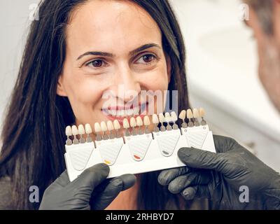 Der Kieferorthopäde des Mannes wählt die Zahnfarbe aus der Schattenführung für die Mandantin bei der Vorbereitung der Zahnaufhellung in der Zahnklinik Stockfoto