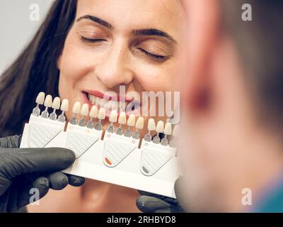 Zahnärztin mit Palette von Implantaten Farbwahl für Veneers für junge weibliche Sitzerin mit geschlossenen Augen in der zahnärztlichen Praxis Stockfoto