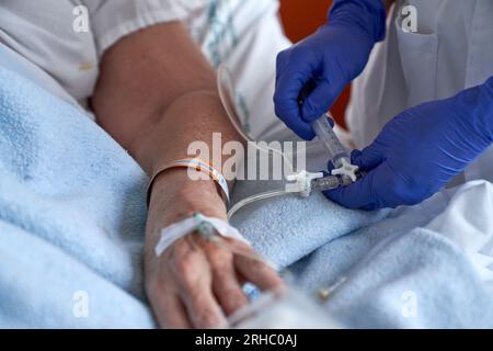 Von oben nicht erkennbare Krankenschwester in Handschuhen, die dem anonymen Patienten intravenöse Injektion mit Spritze und Röhrchen verabreicht Stockfoto
