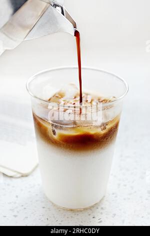 Nahaufnahme des Kaffees, der in ein Glas Milch gegossen wird Stockfoto