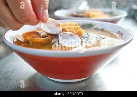 Crop Anonymous Cook serviert leckere heiße Soba-Nudelsuppe mit Muscheln und knusprigem Huhn in der Keramikschüssel in der Restaurantküche Stockfoto