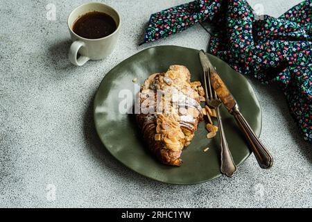 Nahaufnahme eines Mandelcroissants mit einer Tasse schwarzem Kaffee Stockfoto