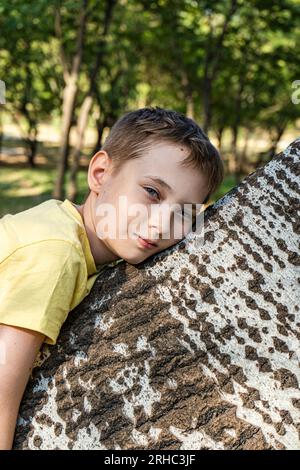 Porträt eines Jungen, der im Sommer auf einem Baumstamm lag, Georgia Stockfoto