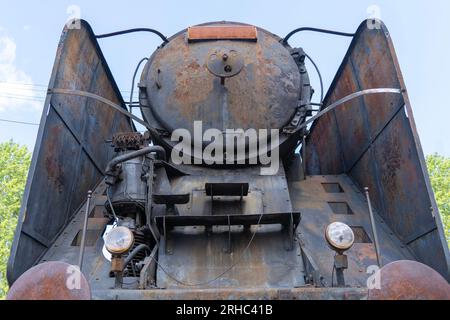 Die Vorderseite einer alten schwarzen, rostigen Dampflokomotive von unten Stockfoto