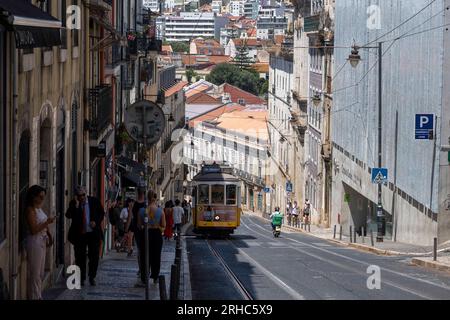 Man sieht Leute in der Nähe einer Straßenbahn in einer der Straßen von Barrio Alto in Lissabon laufen. Stockfoto