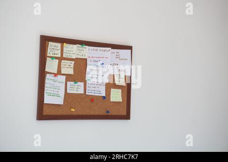 Korktafel mit Haftnotizen mit Motivationssätzen auf einer weißen Wand. Motivationszitate auf Strichnotizen, die auf Korktafeln befestigt sind Stockfoto