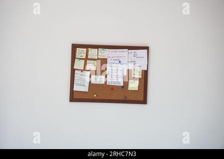 Korktafel mit Haftnotizen mit Motivationssätzen auf einer weißen Wand. Motivationszitate auf Strichnotizen, die auf Korktafeln befestigt sind Stockfoto