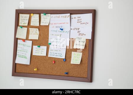 Korktafel mit Haftnotizen mit Motivationssätzen auf einer weißen Wand. Motivationszitate auf Strichnotizen, die auf Korktafeln befestigt sind Stockfoto