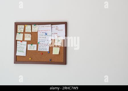 Korktafel mit Haftnotizen mit Motivationssätzen auf einer weißen Wand. Motivationszitate auf Strichnotizen, die auf Korktafeln befestigt sind Stockfoto