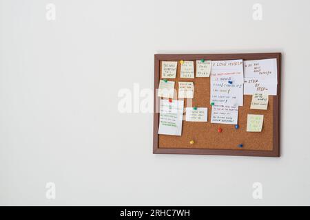 Korktafel mit Haftnotizen mit Motivationssätzen auf einer weißen Wand. Motivationszitate auf Strichnotizen, die auf Korktafeln befestigt sind Stockfoto