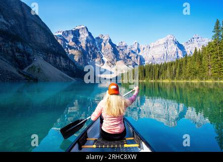 Frau, die im Sommer am frühen Morgen Kanufahren am Moraine Lake im Banff National Park, in den kanadischen Rockies, Alberta, Kanada, macht. Banff-Nationalpark, Al Stockfoto