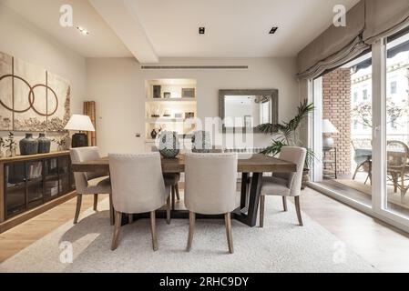 Esstisch aus Holz mit schwarzen Stahlbeinen, Schaufenster aus Holz und Glas, Schiebetüren zur Terrasse und Stühle mit grauen Stoffen Stockfoto