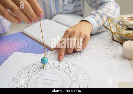 Astrologe mit Zodiakenrad und Pendel zur Schicksalsvorhersage am Tisch, Nahaufnahme. Wahrsagerei Stockfoto