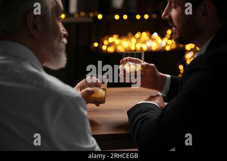 Männer mit Whiskey-Gläsern, die sich an einem Holztisch in der Bar unterhalten Stockfoto