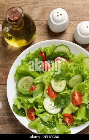 Leckerer Salat, Öl, Salz- und Pfefferstreuer auf Holztisch, flach liegend Stockfoto