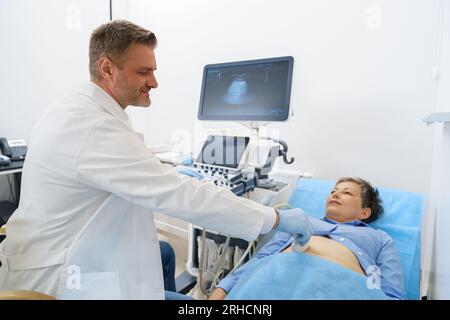 Männlicher Ultraschalltechniker, der für eine Patientin in der medizinischen Klinik Ultraschalluntersuchungen des Abdomens durchführt Stockfoto