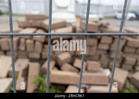 Kettengliederzaun - Haufen Ziegelsteine - gebrochen und gestapelt - bewölkter Himmel - Auto im Hintergrund Stockfoto