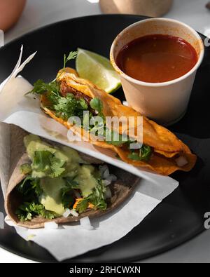 Barbecue-Tacos, mit Conomme an der Seite, mexikanische Tacos in schwarzer Keramikplatte. mexiko lateinamerika Stockfoto