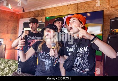 Wacken, Deutschland. 03. Aug. 2023. Festivalbesucher singen Karaoke im Container des Trash Metal Project auf dem Festivalgelände. In Zusammenarbeit mit den Veranstaltern des Festivals versucht das Trash Metal Project, die Themen Abfallvermeidung und Recycling unter die Metallköpfe zu bringen. (Zu dpa-KORR: 'Festivals wollen nachhaltiger werden - aber wie?') Kredit: Axel Heimken/dpa/Alamy Live News Stockfoto