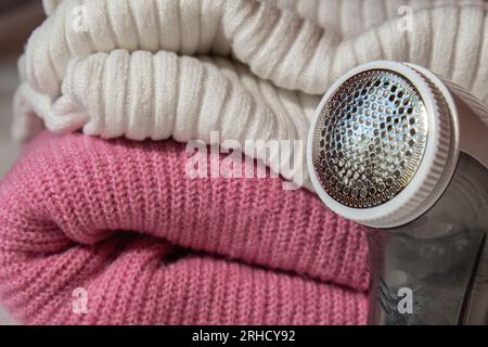 Anti-Pilling-Rasierer. Gerät zum Rasieren von Kleidung. Anti-Plush-Rasierer. Elektrischer tragbarer Pullover, Pille, Entfärbung, Fusselentferner aus pinkfarbenem Acryl- oder Wollpullover. Elektrorasierer nach der Reinigung und aufgefangenen Fusseln. Ein Pullover aus der Nahaufnahme. Alte gebrauchte Kleidung mit Pillen. Stockfoto